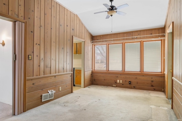 unfurnished bedroom featuring visible vents, carpet flooring, vaulted ceiling, wood walls, and ceiling fan