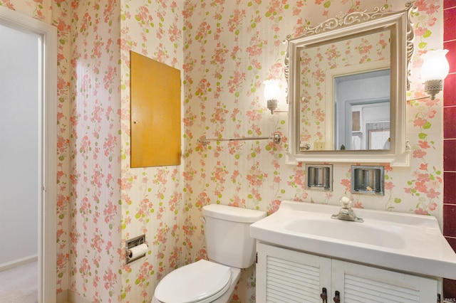 bathroom featuring toilet, vanity, and wallpapered walls