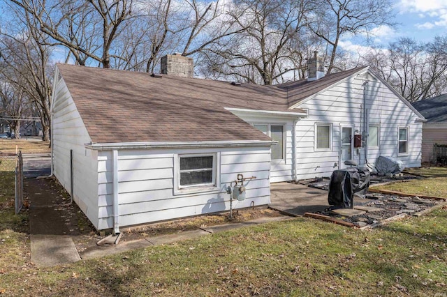 back of property featuring a patio area, roof with shingles, a lawn, and a chimney