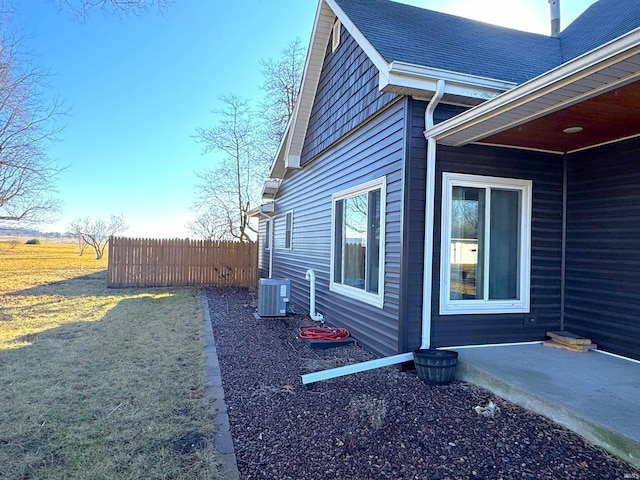 view of side of home featuring central AC, a shingled roof, a lawn, and fence