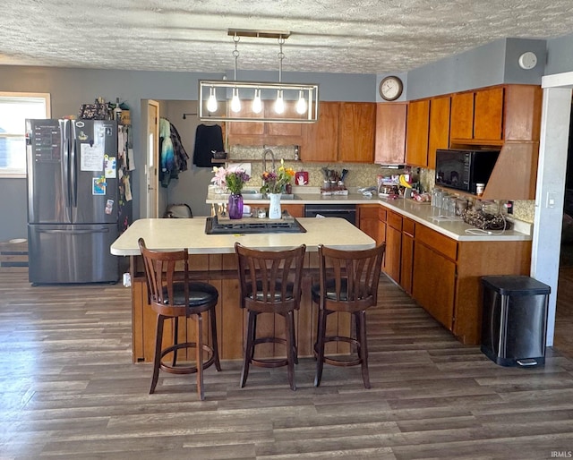 kitchen with black microwave, dark wood-type flooring, light countertops, freestanding refrigerator, and brown cabinets