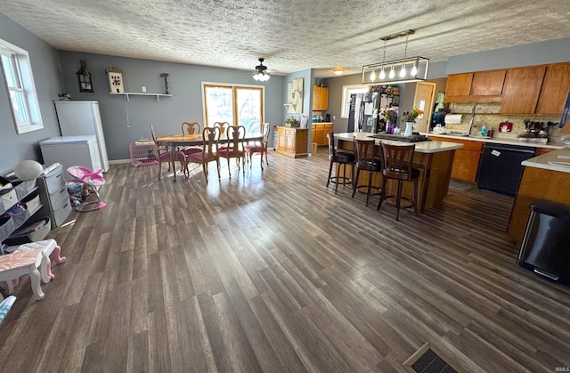 kitchen with black dishwasher, dark wood-style floors, brown cabinets, a center island, and light countertops