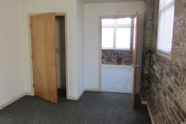 unfurnished bedroom with dark colored carpet, baseboards, and brick wall