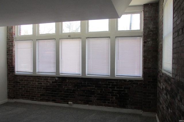 carpeted empty room featuring brick wall