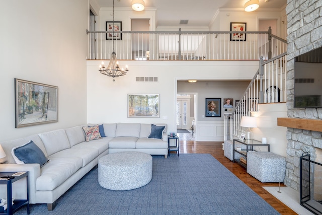 living area with visible vents, ornamental molding, wood finished floors, stairs, and a stone fireplace