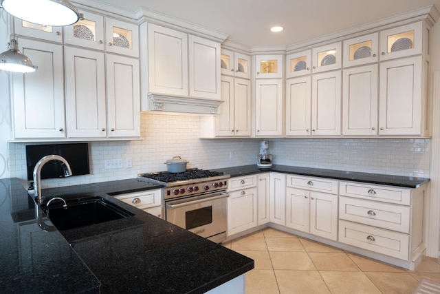 kitchen featuring light tile patterned floors, high end stove, premium range hood, pendant lighting, and a sink