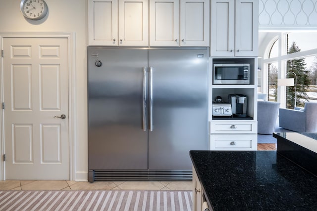 kitchen featuring dark stone counters, white cabinets, light tile patterned floors, and built in appliances