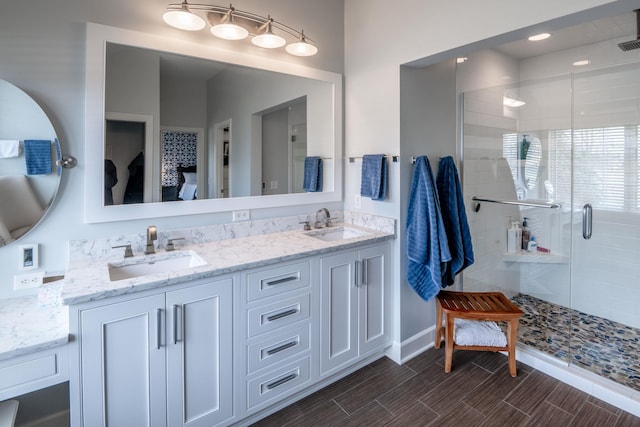 full bathroom with double vanity, a shower stall, wood tiled floor, and a sink