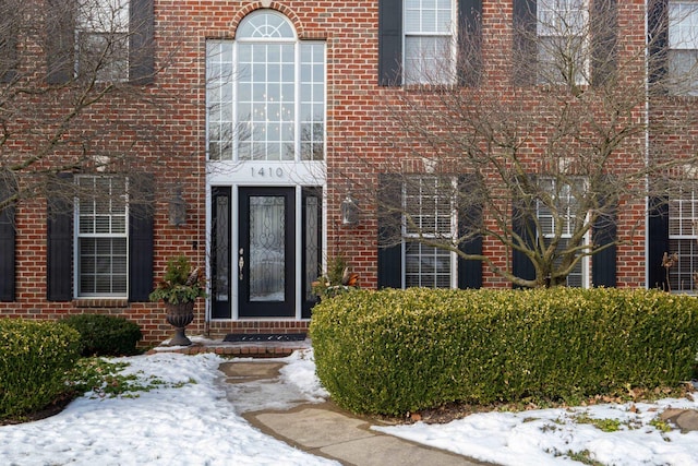 snow covered property entrance with brick siding