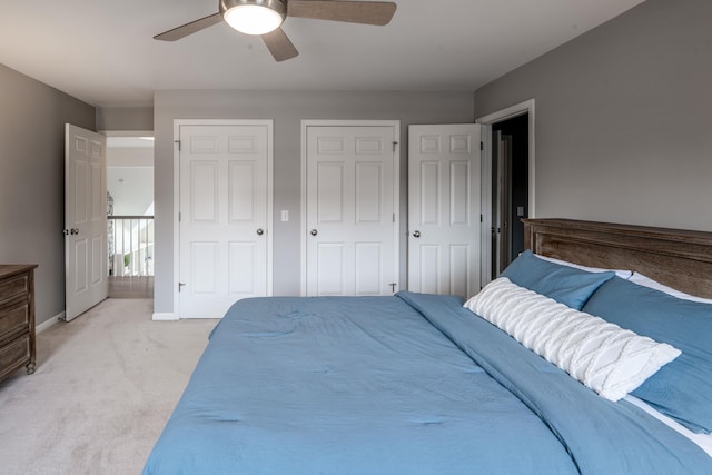 bedroom featuring light carpet, ceiling fan, two closets, and baseboards