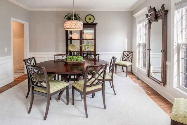 dining room featuring a wainscoted wall, light wood-style flooring, and ornamental molding