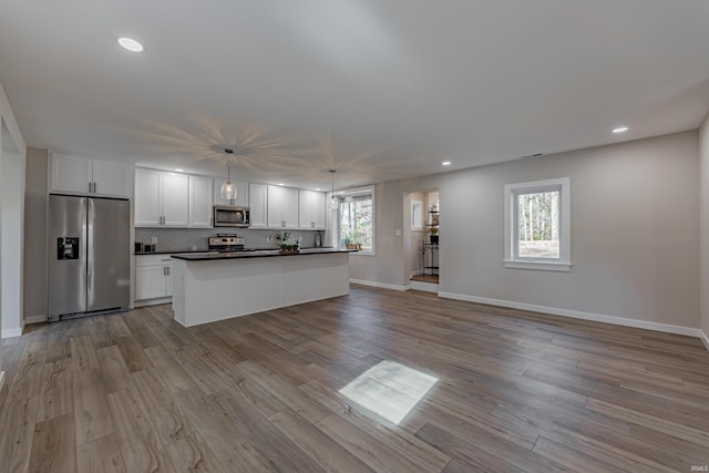 kitchen with stainless steel appliances, dark countertops, wood finished floors, and tasteful backsplash