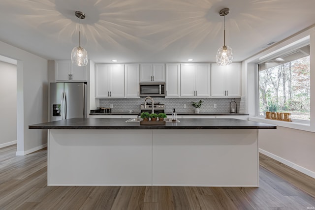 kitchen with appliances with stainless steel finishes, white cabinetry, a center island with sink, and tasteful backsplash