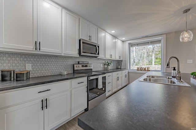 kitchen featuring stainless steel appliances, dark countertops, tasteful backsplash, white cabinetry, and a sink