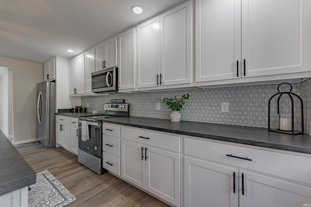 kitchen with dark countertops, light wood-style flooring, appliances with stainless steel finishes, and white cabinets