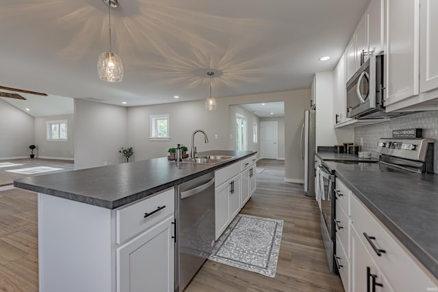 kitchen featuring stainless steel appliances, dark countertops, tasteful backsplash, a sink, and an island with sink