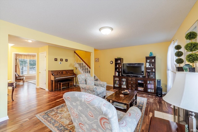 living room featuring a textured ceiling, stairs, baseboards, and wood finished floors