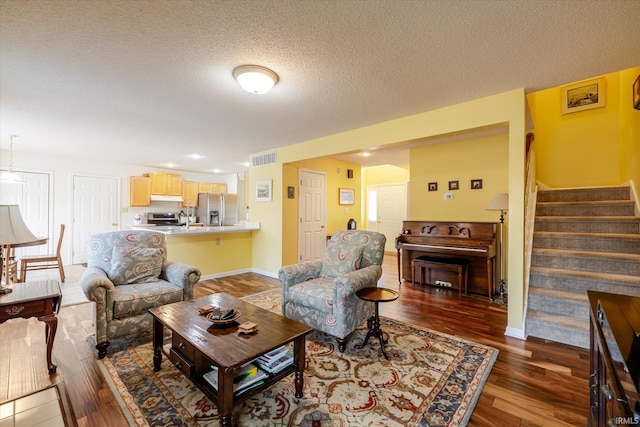 living area featuring visible vents, a textured ceiling, wood finished floors, baseboards, and stairs