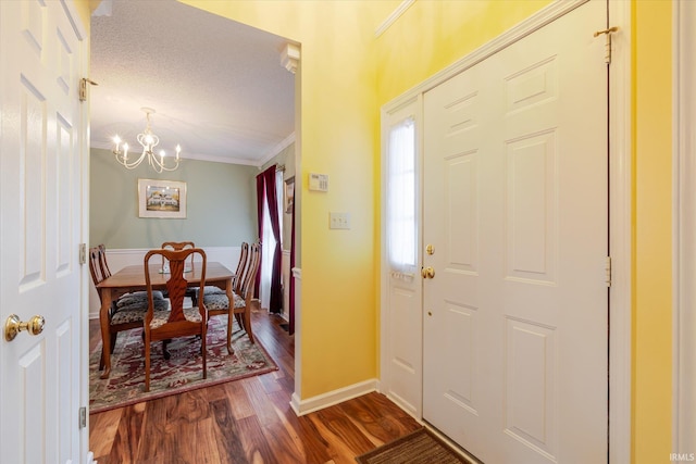 foyer entrance with baseboards, dark wood-style floors, a textured ceiling, crown molding, and a notable chandelier