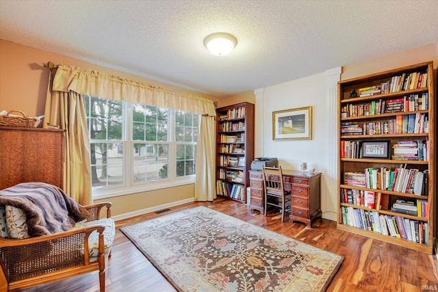 office space featuring a textured ceiling, wood finished floors, visible vents, and baseboards