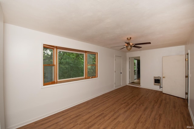 empty room with baseboards, plenty of natural light, heating unit, and wood finished floors