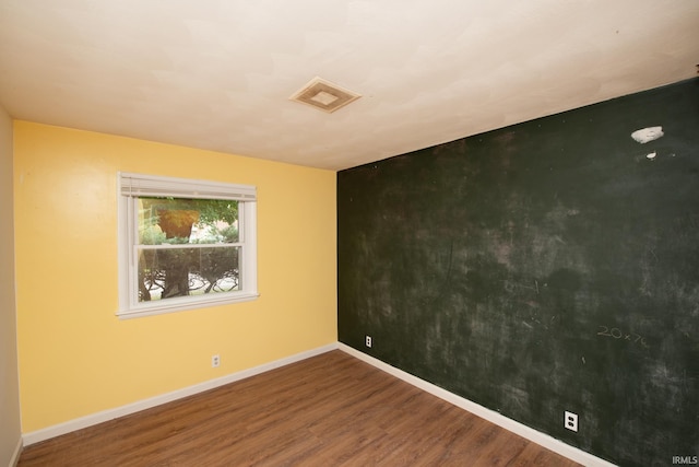 spare room with an accent wall, wood finished floors, visible vents, and baseboards