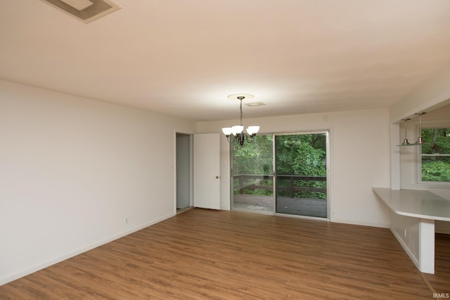 unfurnished dining area with baseboards, wood finished floors, visible vents, and an inviting chandelier