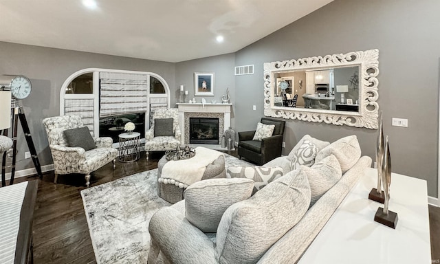 living room featuring lofted ceiling, visible vents, a premium fireplace, wood finished floors, and baseboards