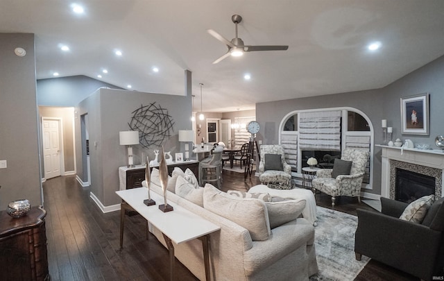 living room featuring a high end fireplace, a ceiling fan, lofted ceiling, dark wood-type flooring, and recessed lighting