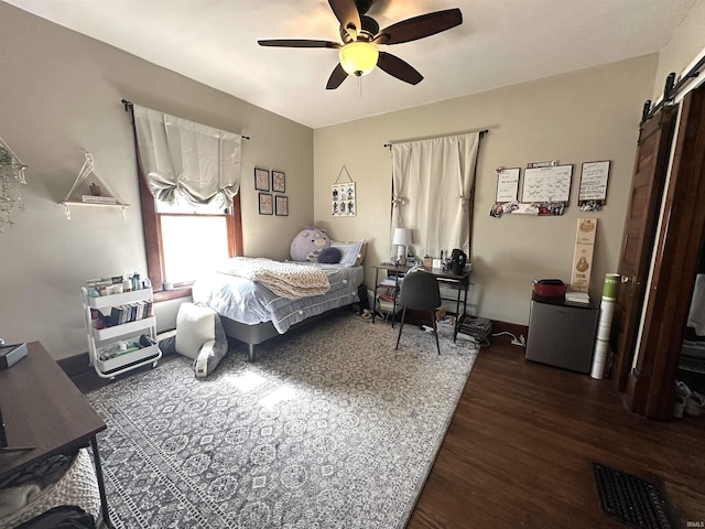 bedroom with a barn door, a ceiling fan, and wood finished floors