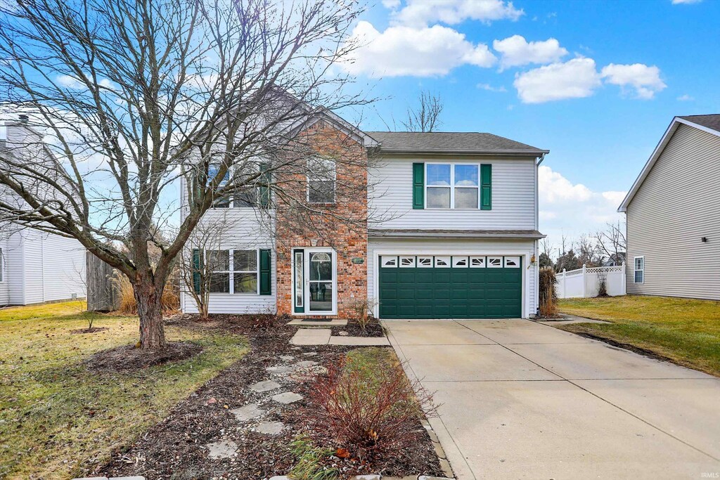 traditional-style home featuring a garage, concrete driveway, fence, a front lawn, and brick siding