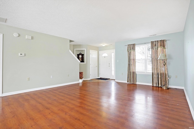 unfurnished living room with a textured ceiling, baseboards, and wood finished floors