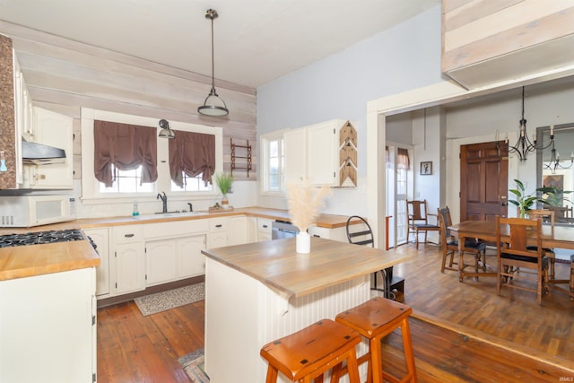 kitchen featuring dark wood-style flooring, wooden counters, white microwave, white cabinets, and a sink