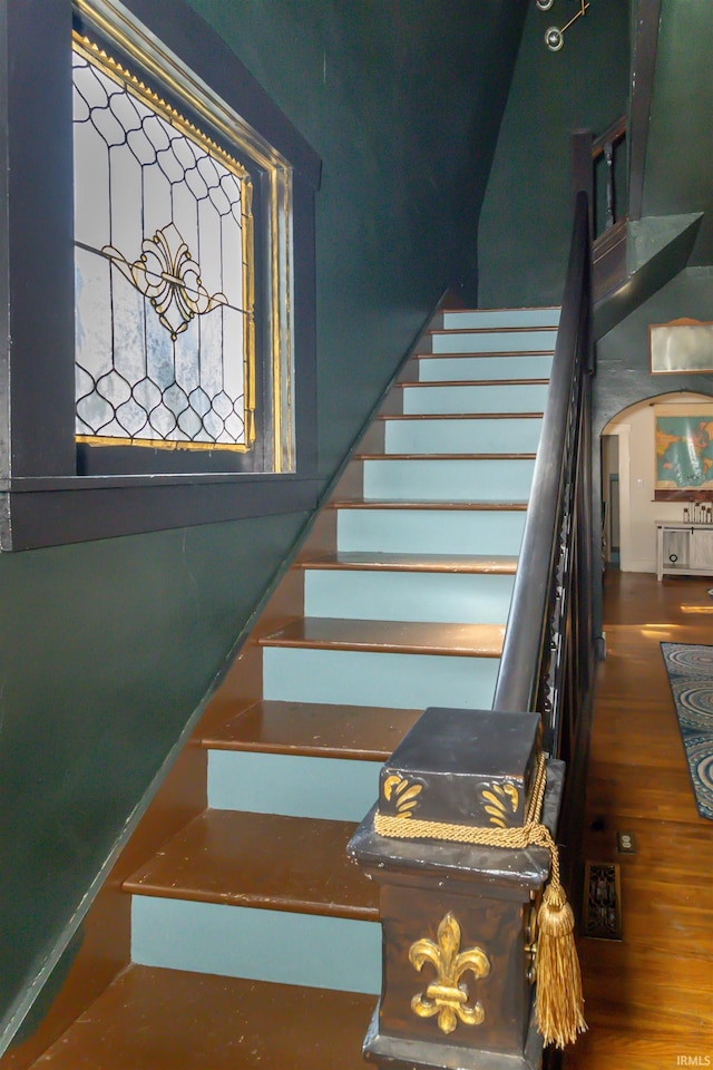 staircase featuring arched walkways and wood finished floors