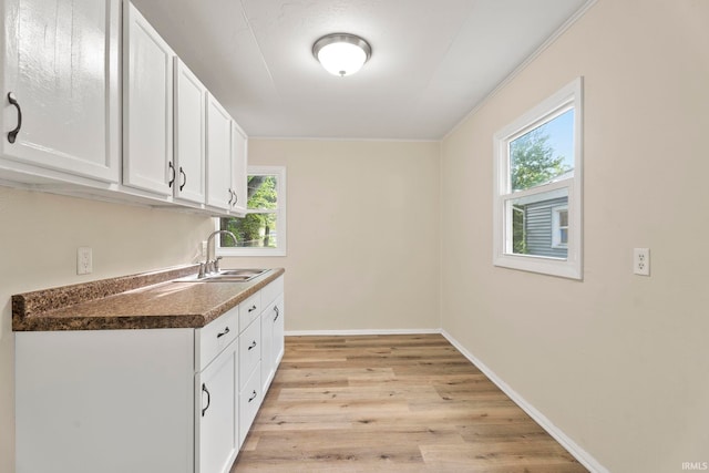 kitchen featuring light wood finished floors, dark countertops, white cabinets, a sink, and baseboards