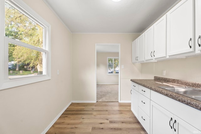 kitchen featuring dark countertops, light wood-style flooring, white cabinets, a sink, and baseboards