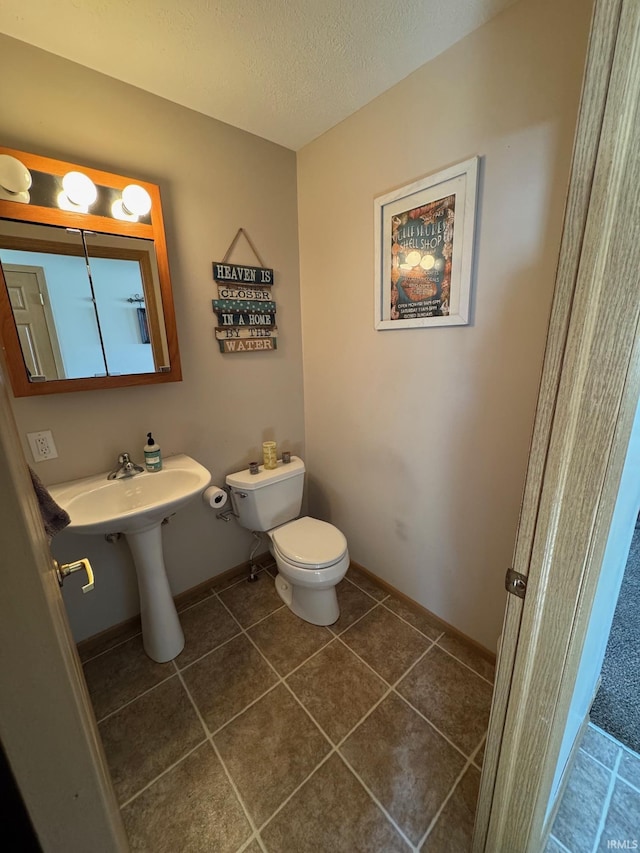 half bath with toilet, tile patterned flooring, a sink, and a textured ceiling