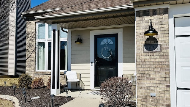 doorway to property with a shingled roof, brick siding, and a garage