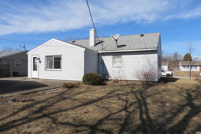 back of property with a shingled roof, a chimney, and a patio