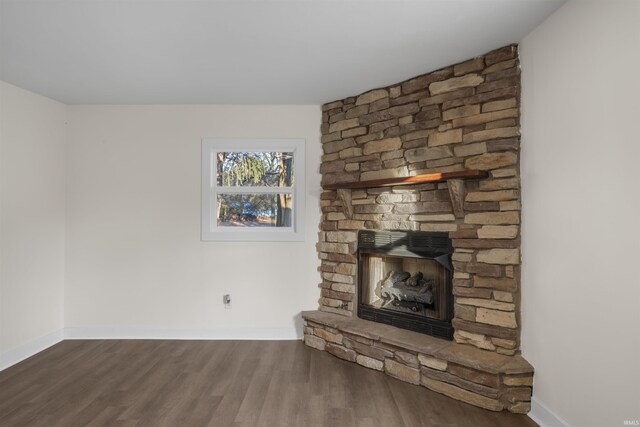 unfurnished living room featuring a stone fireplace, baseboards, and wood finished floors