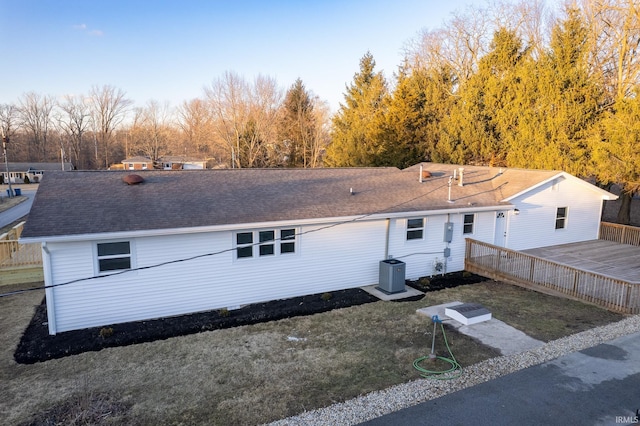 back of property with cooling unit, roof with shingles, a lawn, and a deck