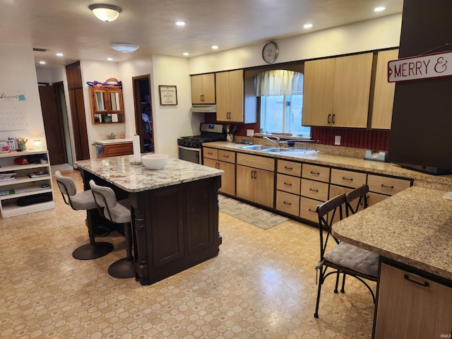 kitchen featuring stainless steel gas range, a kitchen breakfast bar, a sink, and light floors