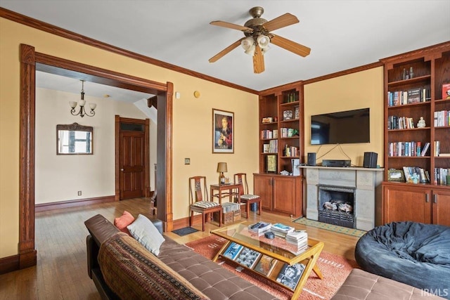 living room featuring baseboards, built in features, wood finished floors, crown molding, and a fireplace