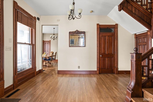 entryway with an inviting chandelier, stairs, visible vents, and wood finished floors