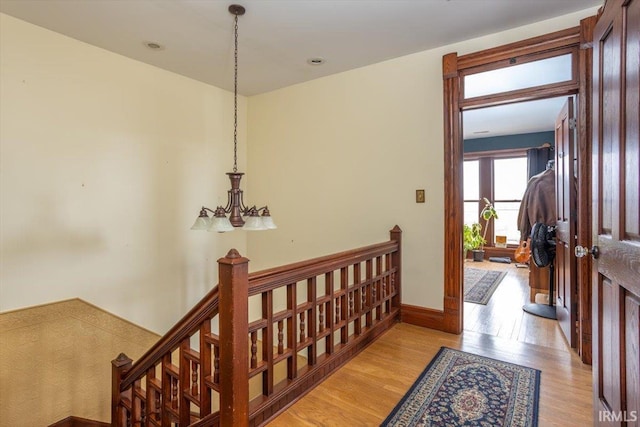 hall featuring baseboards, an inviting chandelier, an upstairs landing, and light wood-style floors