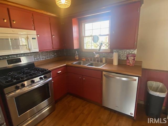 kitchen featuring decorative backsplash, appliances with stainless steel finishes, wood finished floors, light countertops, and a sink