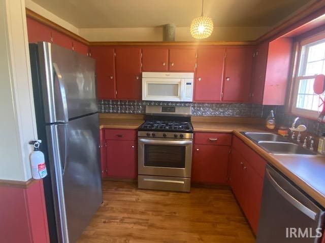 kitchen with light wood-style flooring, a sink, appliances with stainless steel finishes, red cabinets, and tasteful backsplash