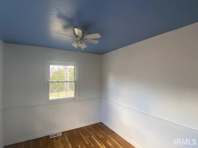 empty room with a ceiling fan, dark wood-style flooring, visible vents, and baseboards