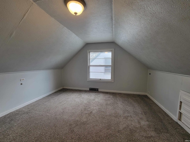additional living space featuring lofted ceiling, a textured ceiling, baseboards, visible vents, and carpet floors