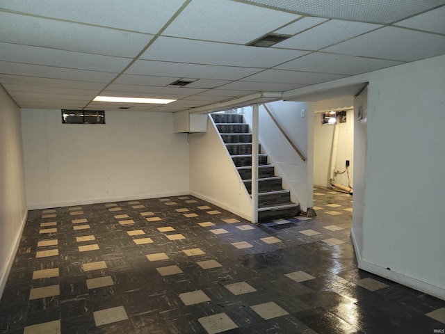 finished basement featuring a paneled ceiling, stairs, visible vents, and dark floors